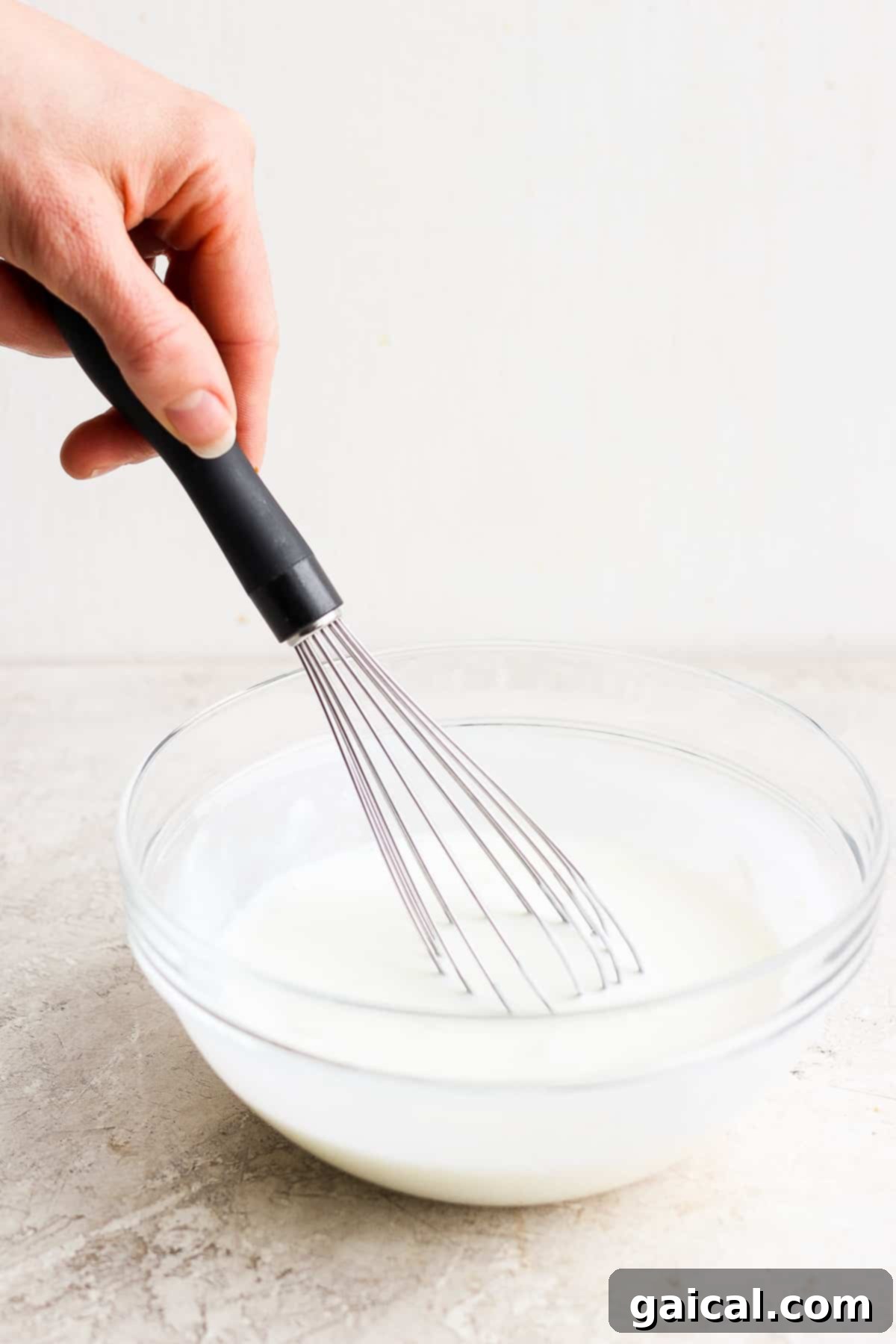 Whisking the ingredients for homemade ranch dressing. A person whisking ranch dressing in a glass bowl.