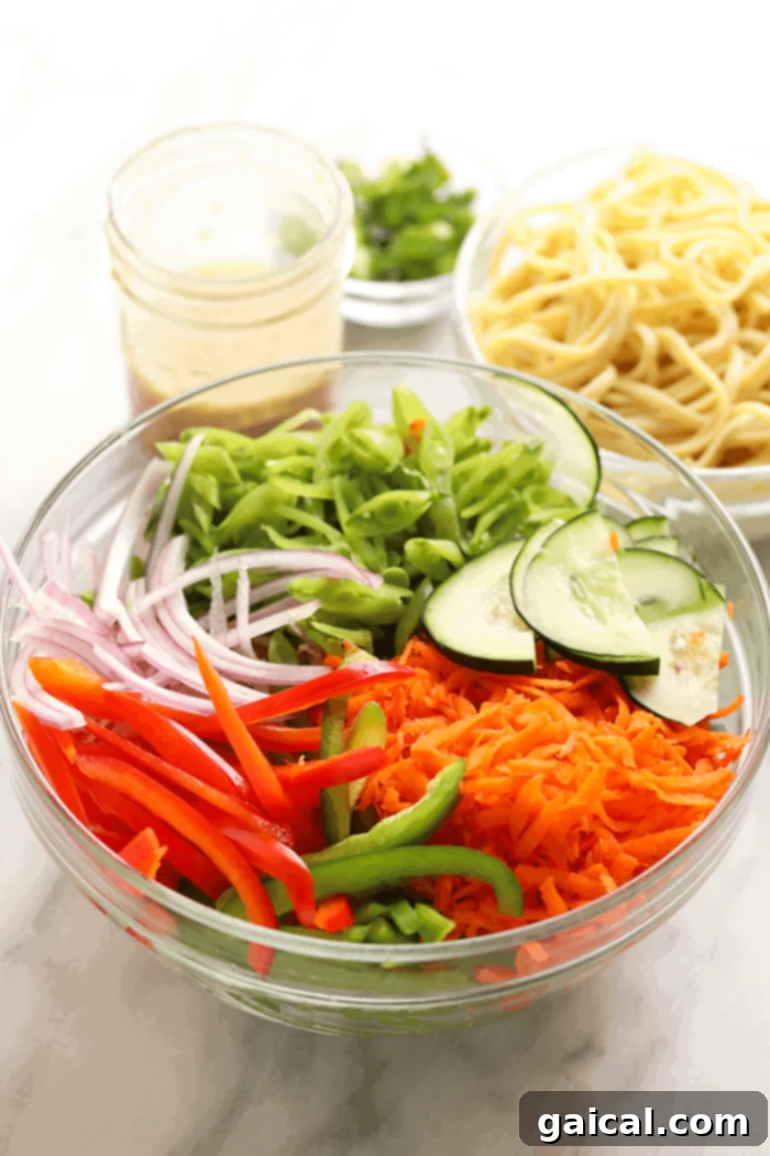 A vibrant display of fresh ingredients for Asian noodle salad, including colorful bell peppers, carrots, cucumbers, and a bowl of noodles, ready for preparation.