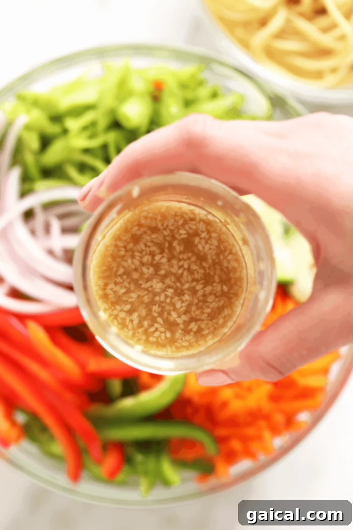 A mason jar filled with a rich, amber-colored sesame dressing, ready to be poured over an Asian noodle salad.