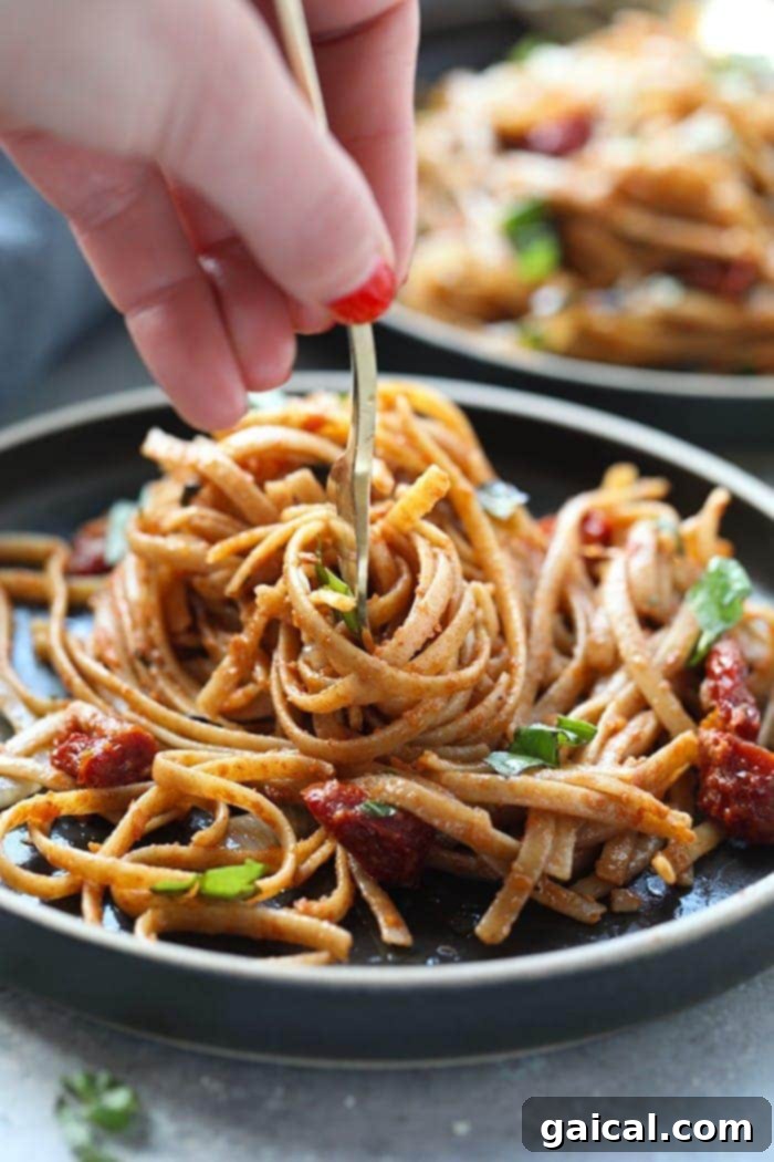A fork twirling whole wheat sun dried tomato pasta, showing the rich sauce clinging to the noodles, garnished with fresh basil.