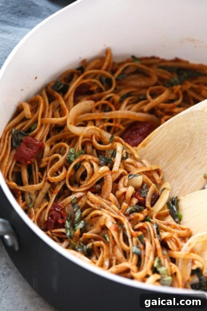 Sun dried tomato pasta with whole wheat noodles simmering in a large pan, showing the rich red color of the sauce.