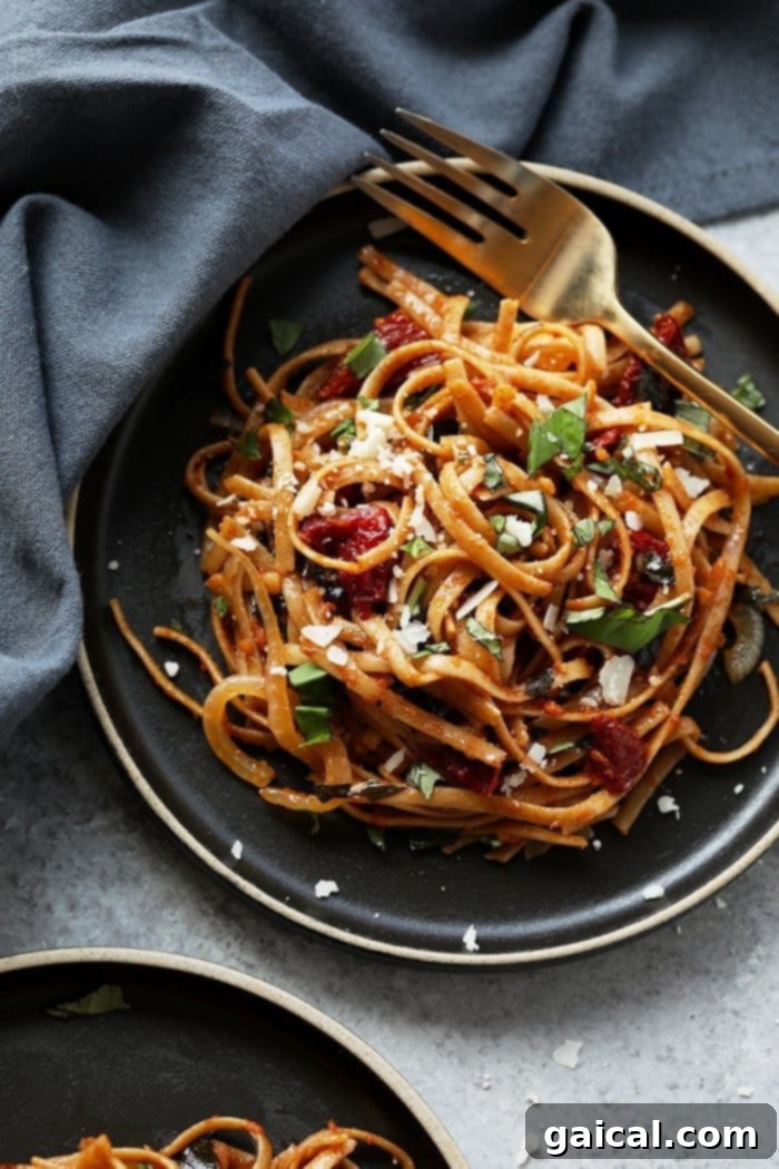 A close-up of vegetarian sun dried tomato pasta, generously garnished with fresh parmesan cheese and basil leaves.