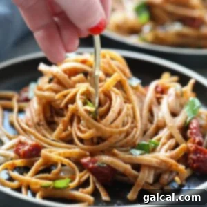 A person holding a fork with a mouthful of Sun Dried Tomato Basil Pasta, highlighting the texture and sauciness of the dish.