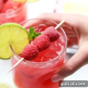 A person holding a raspberry mojito garnished with lime and fresh mint.