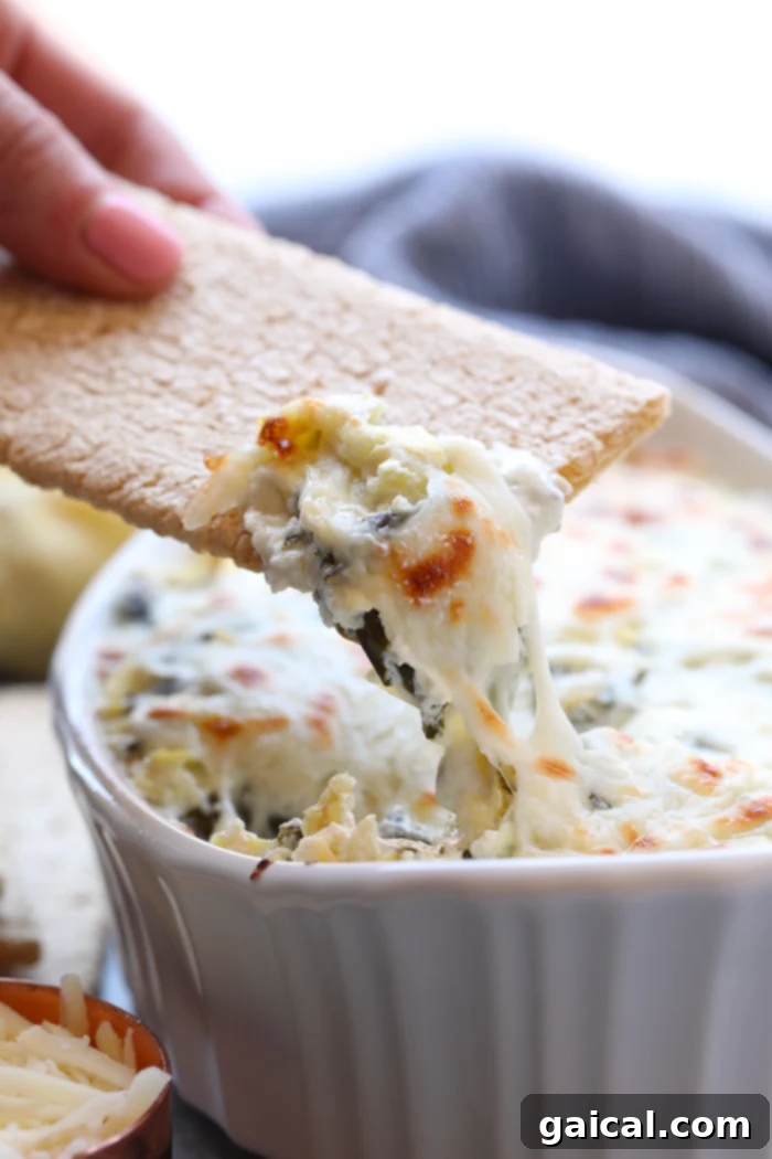 A vibrant, golden-brown baked spinach artichoke dip in a rustic baking dish, with a spoon ready for serving, highlighting its creamy texture and cheesy top.