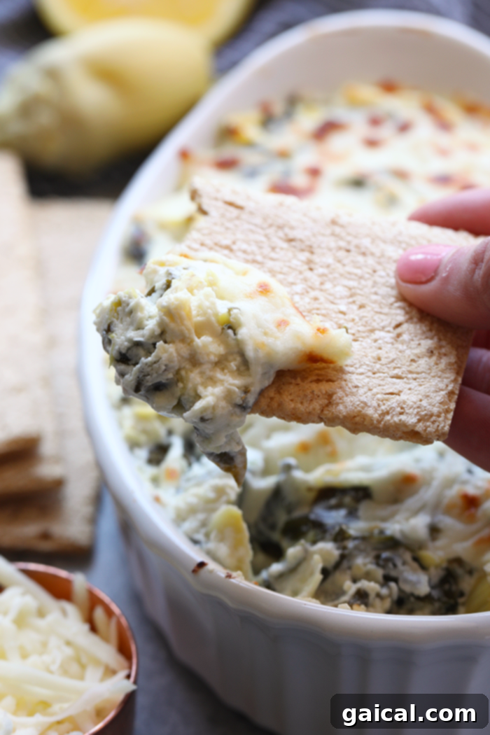 A cracker generously loaded with creamy, homemade spinach artichoke dip, showcasing its delightful texture, poised for a delicious bite.