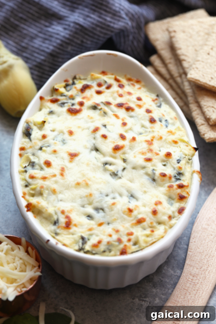 A bowl of freshly baked, warm spinach artichoke dip, garnished with fresh parsley, surrounded by an assortment of dippers like crackers and colorful fresh vegetables, inviting to be enjoyed.