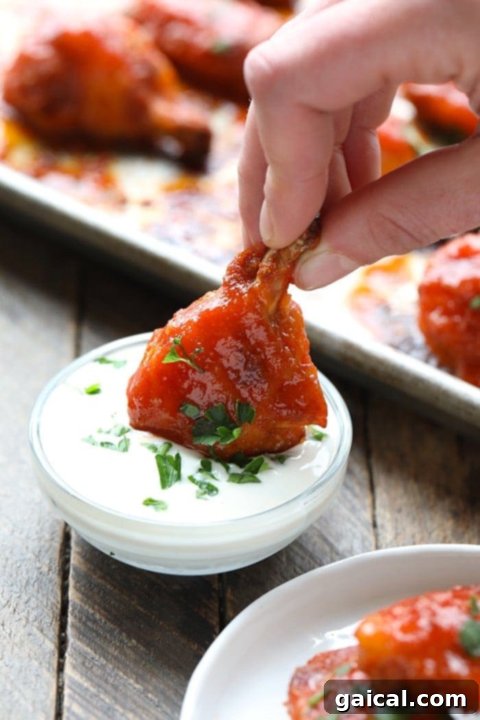 Dipping a Crispy Baked Buffalo Wing A perfectly baked buffalo chicken wing being dipped into a creamy, healthy yogurt-based sauce, showcasing its crispy texture and delicious coating.