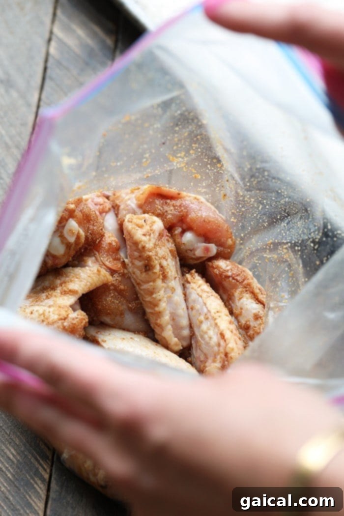 Chicken Wings Marinating with Dry Rub Unbaked chicken wings are shown in a clear ziploc bag, coated with a flavorful dry rub of spices, ready for baking.