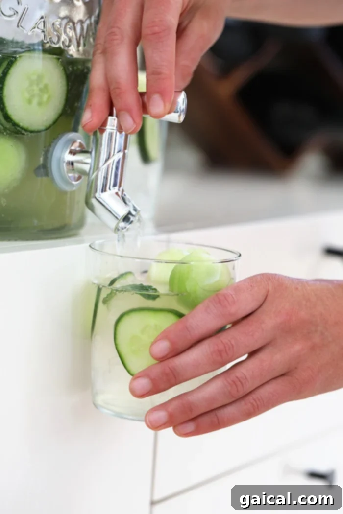 Large Batch Cucumber Vodka Cocktail for Summer Parties A refreshing cucumber vodka drink dispensed into a glass, garnished with vibrant cucumber slices and a mint sprig, set against a bright summer backdrop. This inviting image highlights the drink's crisp and cool nature, perfect for outdoor gatherings and warm weather enjoyment.