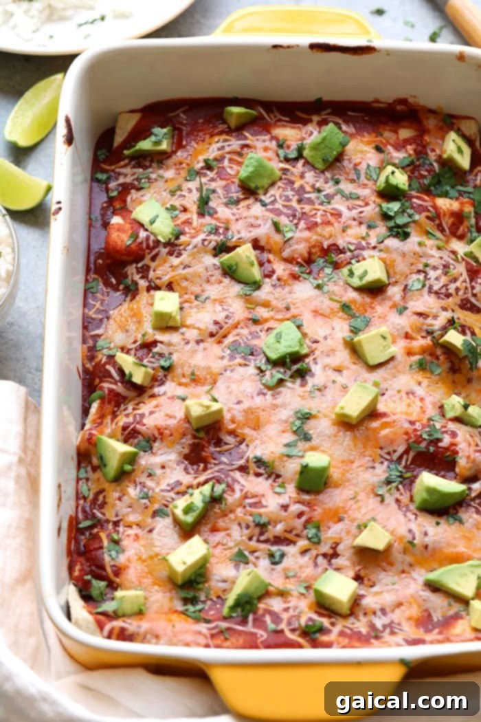Baked Healthy Enchiladas with Cheese and Avocado A baking dish filled with golden-brown healthy chicken and sweet potato enchiladas, topped with melted cheddar cheese and fresh avocado slices.