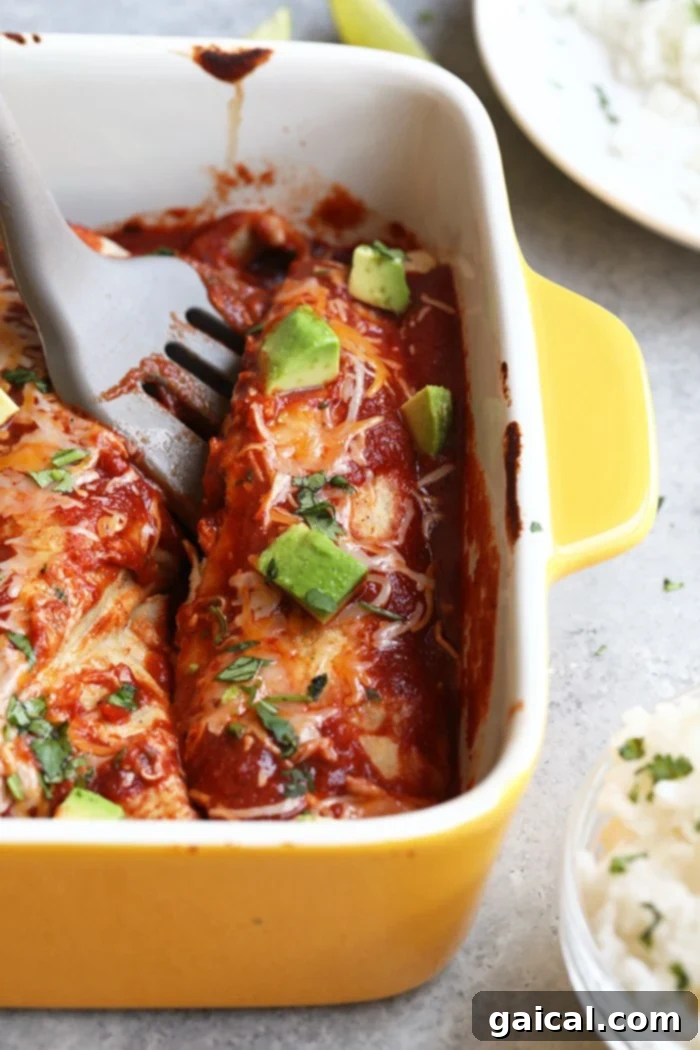 Serving Healthy Chicken Enchiladas A spatula scooping a single healthy chicken and sweet potato enchilada from a yellow baking dish, showing the delicious filling.