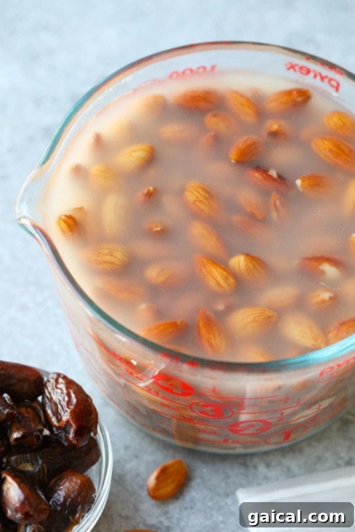 Raw almonds soaking in a clear bowl of filtered water on a kitchen counter, illustrating the crucial first step for softening them before blending into milk.