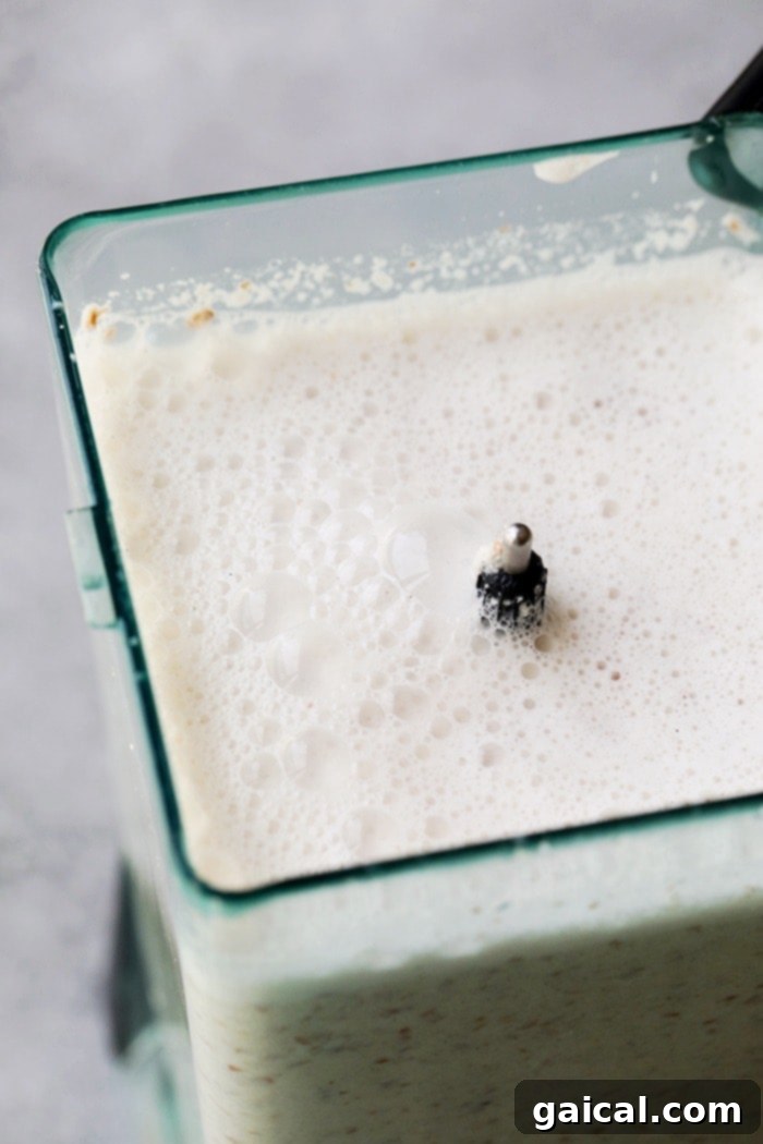 Creamy almond milk mixture being thoroughly blended in a high-speed blender, showing the process before straining.