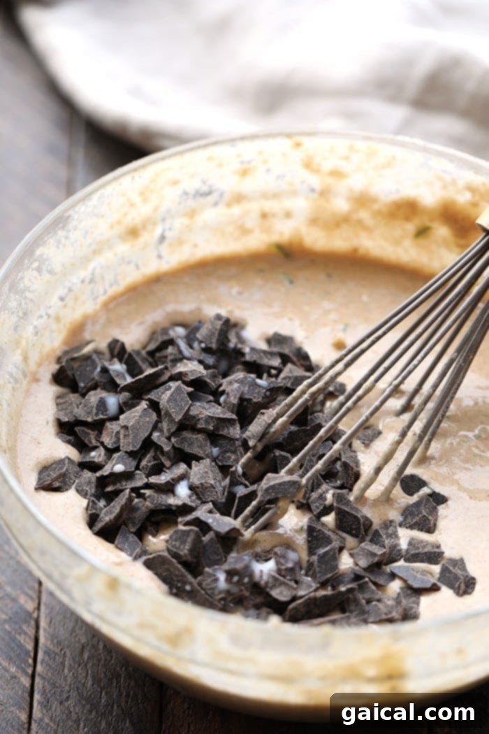 Smooth and thick zucchini waffle batter, perfectly mixed and ready for the waffle iron, promising fluffy results. Thick, rich zucchini waffle batter in a white bowl, ready to be poured into the waffle iron for cooking.