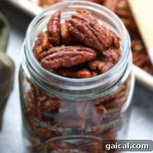 Roasted pecans displayed in a glass jar with a wooden spoon.
