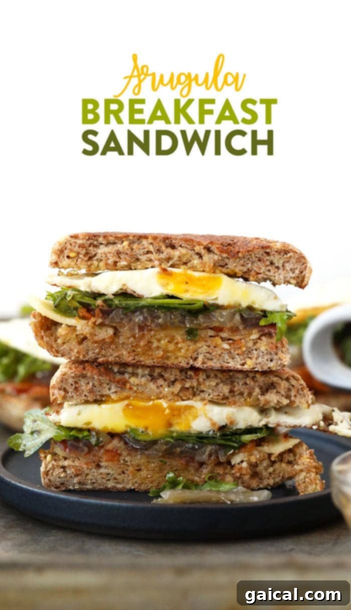 A vibrant Arugula Breakfast Sandwich with caramelized onions, bacon, and a fried egg on a toasted English muffin, ready to be enjoyed.