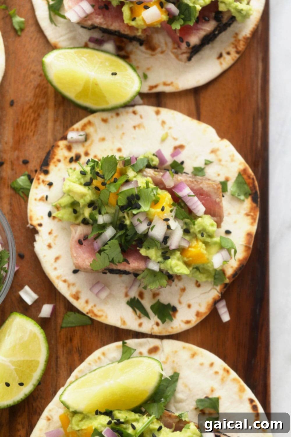 Gorgeous Ahi Tuna Tacos with Seared Tuna and Mango Guacamole Delicious Ahi Tuna Tacos served on a rustic cutting board, garnished with fresh cilantro and lime wedges.
