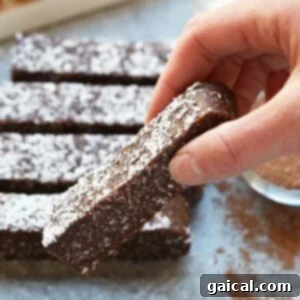 Effortless Chocolate Coconut Energy Bars 6 a person is dipping a chocolate bar