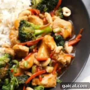 A plate with ginger chicken stir-fry, featuring broccoli, carrots, and cashews next to white rice.