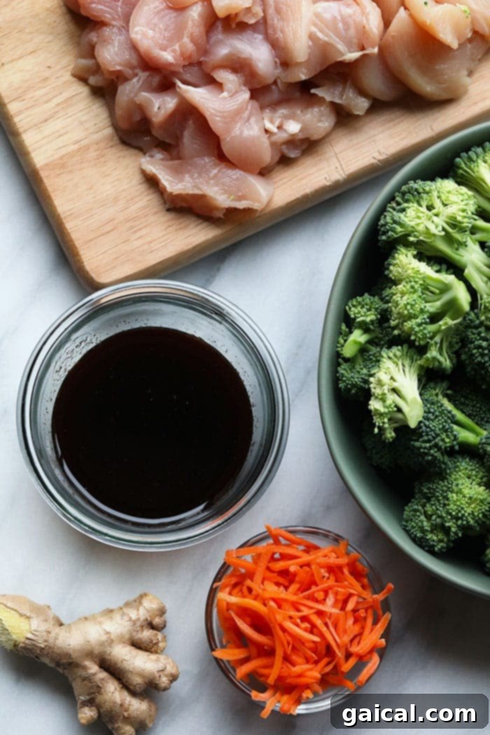 Quick and Easy Chicken Stir Fry 3 Fresh ingredients laid out: bowls of minced ginger, soy sauce, vibrant broccoli florets, shredded carrots, and raw chicken breast, ready for a homemade stir fry.