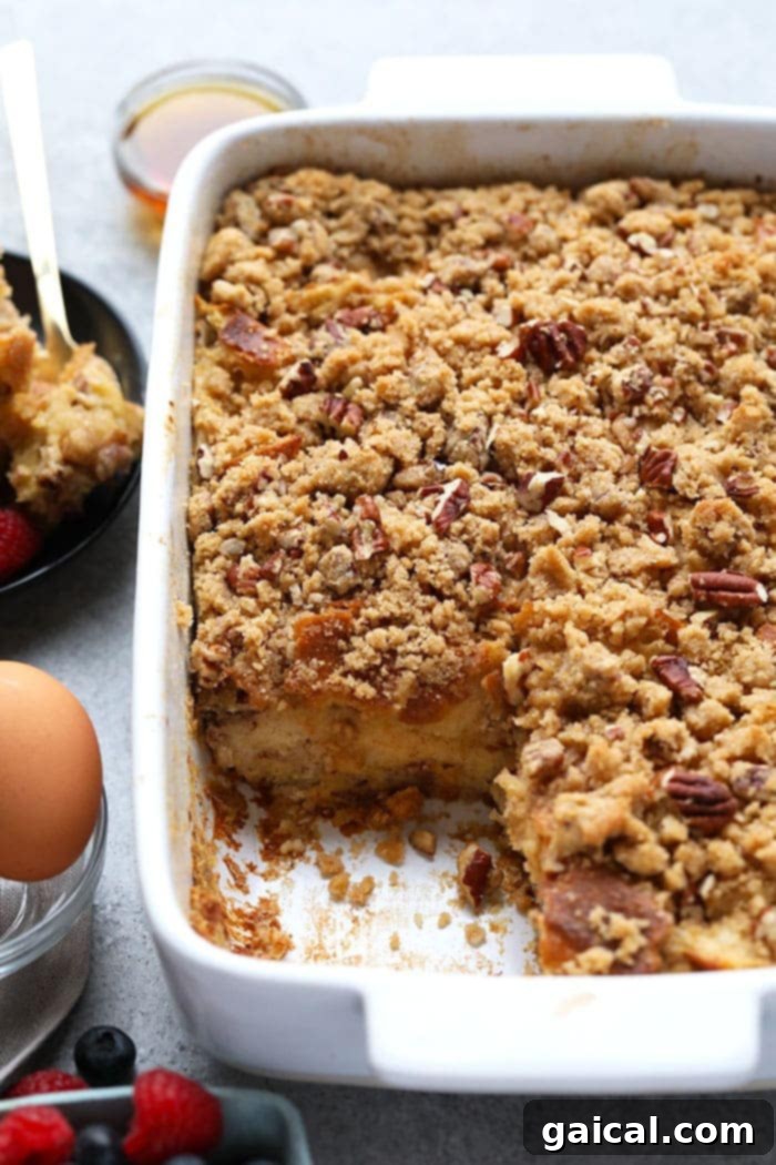 This overnight baked French toast recipe is a crowd-pleasing breakfast that can be made ahead of time for easy preparation in the morning! It's served with a delicious streusel topping and maple syrup. A slice removed from a baked overnight French toast casserole, revealing its soft, custardy interior and golden-brown exterior.