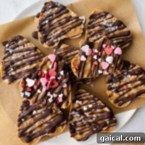 Heart-shaped peanut butter cups drizzled with chocolate and festive Valentine's sprinkles, arranged artfully on a parchment-lined plate.