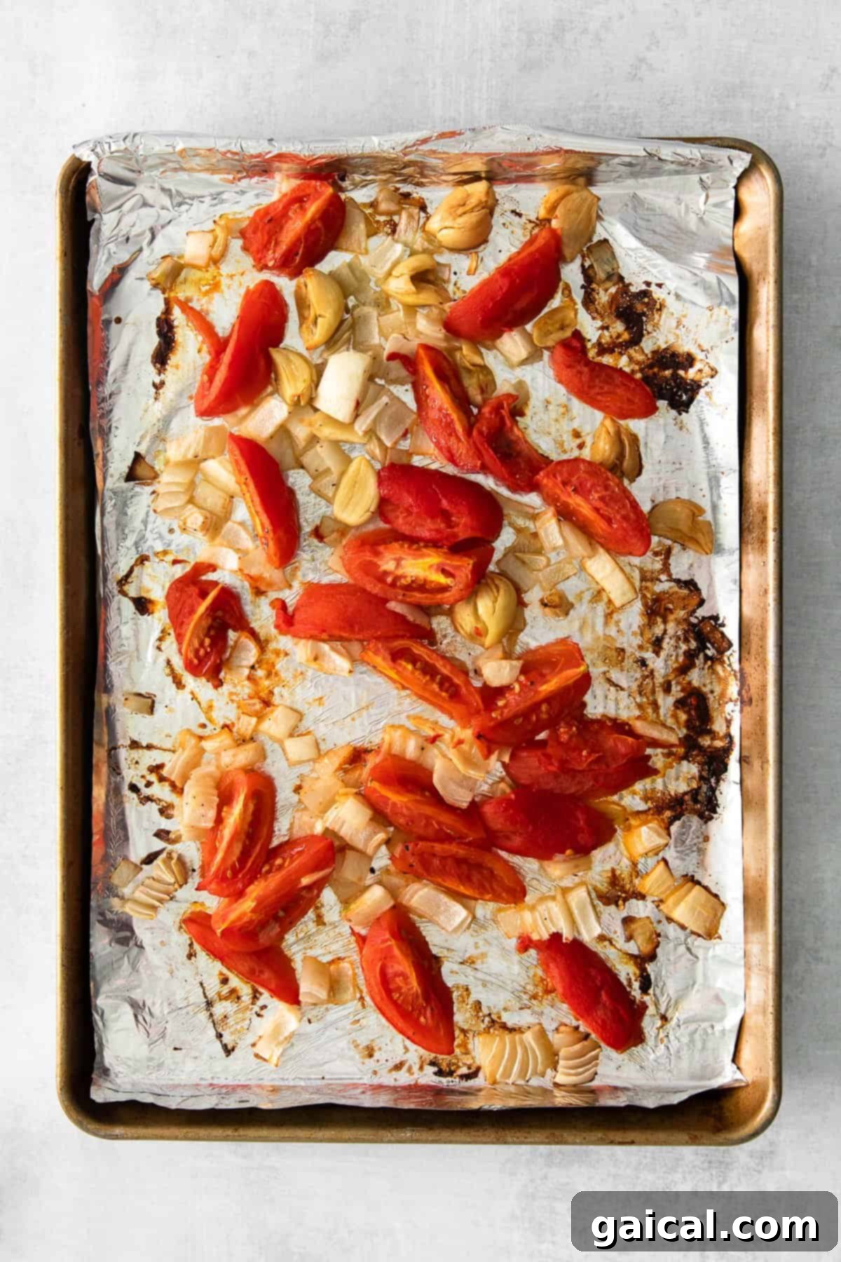 Roasted tomatoes, onions, and garlic on a baking pan for vegan pasta sauce