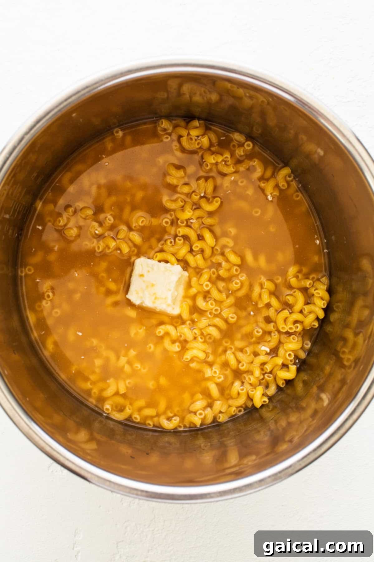 Protein-Powered Instant Pot Mac 3 Macaroni noodles, a pat of butter, and chicken broth simmering inside an Instant Pot, showing the initial cooking stage.