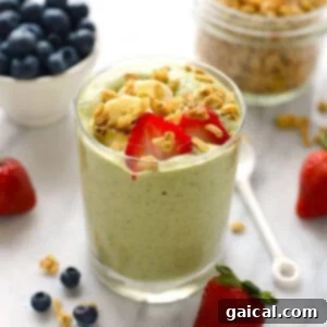 A vibrant green smoothie topped with fresh berries in a glass, ready to drink.