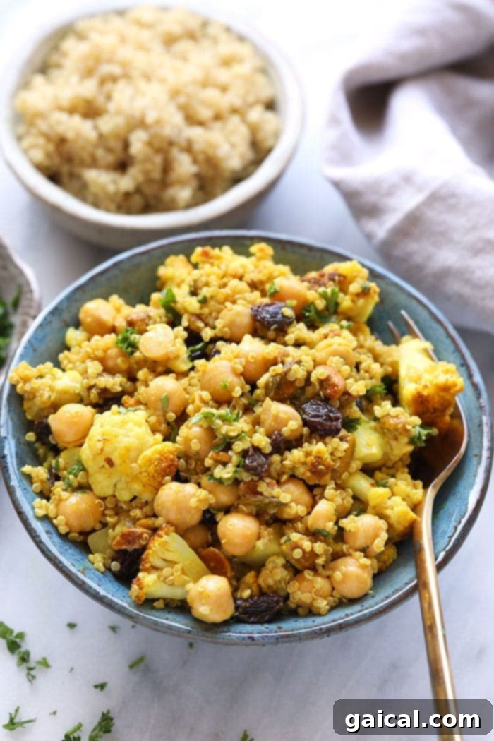 A vibrant bowl of Golden Roasted Cauliflower and Quinoa Salad, featuring tender roasted cauliflower florets, fluffy quinoa, chickpeas, pistachios, and a drizzle of creamy tahini dressing.
