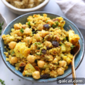 A bowl of couscous with golden roasted cauliflower and chickpeas, garnished with raisins.
