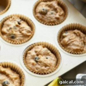 A muffin tin with paper liners generously filled with healthy blueberry muffin batter, showcasing a rich, thick texture ready for the oven.