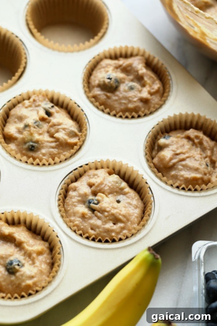 These healthy blueberry muffins are quick to prepare, perfect for picnics, or as a nutritious snack the whole family will adore! Muffin tin lined with paper cups and filled with healthy blueberry muffin batter, ready for baking.