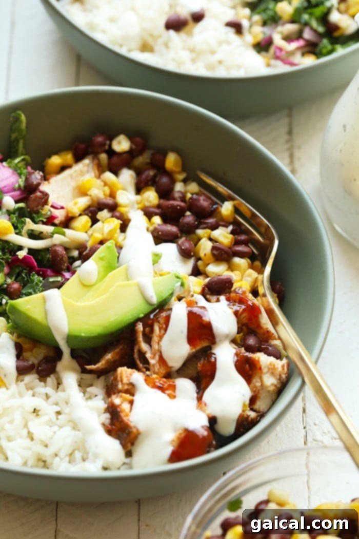Drizzle your favorite dressing over these bbq chicken bowls! They are packed with protein and a healthy dinner option for the week! Two vibrant, finished BBQ chicken bowls on a rustic wooden board, each filled with grilled chicken, rice, black beans, corn, fresh slaw, and sliced avocado, drizzled with dressing.