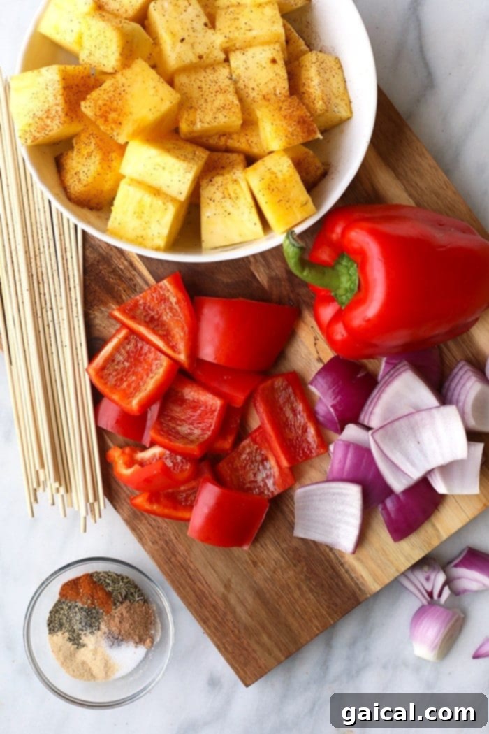 Fresh ingredients for Grilled Pineapple and Jerk Chicken Kebabs laid out: chicken breast, pineapple chunks, red bell peppers, and red onion, alongside a bowl of jerk seasoning.