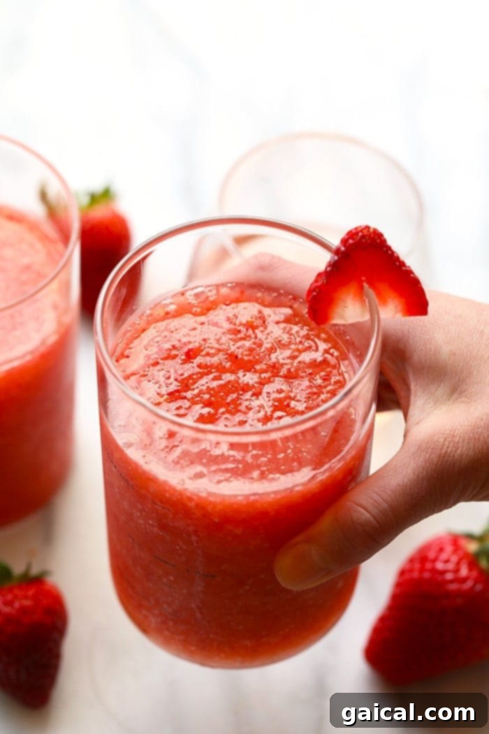Enjoying Freshly Made Strawberry Peach Frosé A hand holding a perfectly blended glass of strawberry peach frosé, featuring a delicate pink hue and smooth texture, ready to be enjoyed on a warm day.