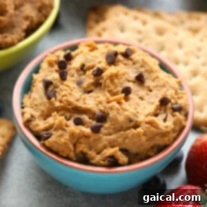 A bowl of peanut butter hummus with strawberries and crackers, topped with edible cookie dough.