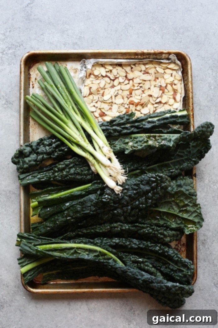 Cookie sheet prepared with fresh kale, green onions, and slivered almonds, ready for grilling, highlighting the ease of preparation for this delicious summer salad.