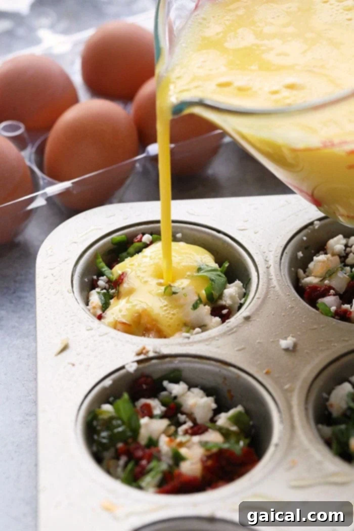 Garden Green Egg Cups 3 Pouring whisked eggs into a muffin tin filled with a vibrant mix of spinach, sun-dried tomatoes, and feta cheese, ready for baking into healthy breakfast muffins.