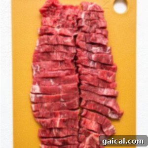 Thinly sliced raw flank steak strips arranged on a cutting board, ready for a stir-fry.