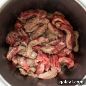 Partially seared beef strips cooking in olive oil inside an Instant Pot.