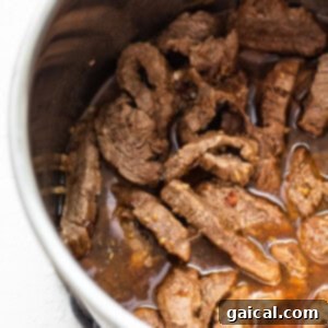 Cooked beef strips immersed in a rich sauce inside an Instant Pot.