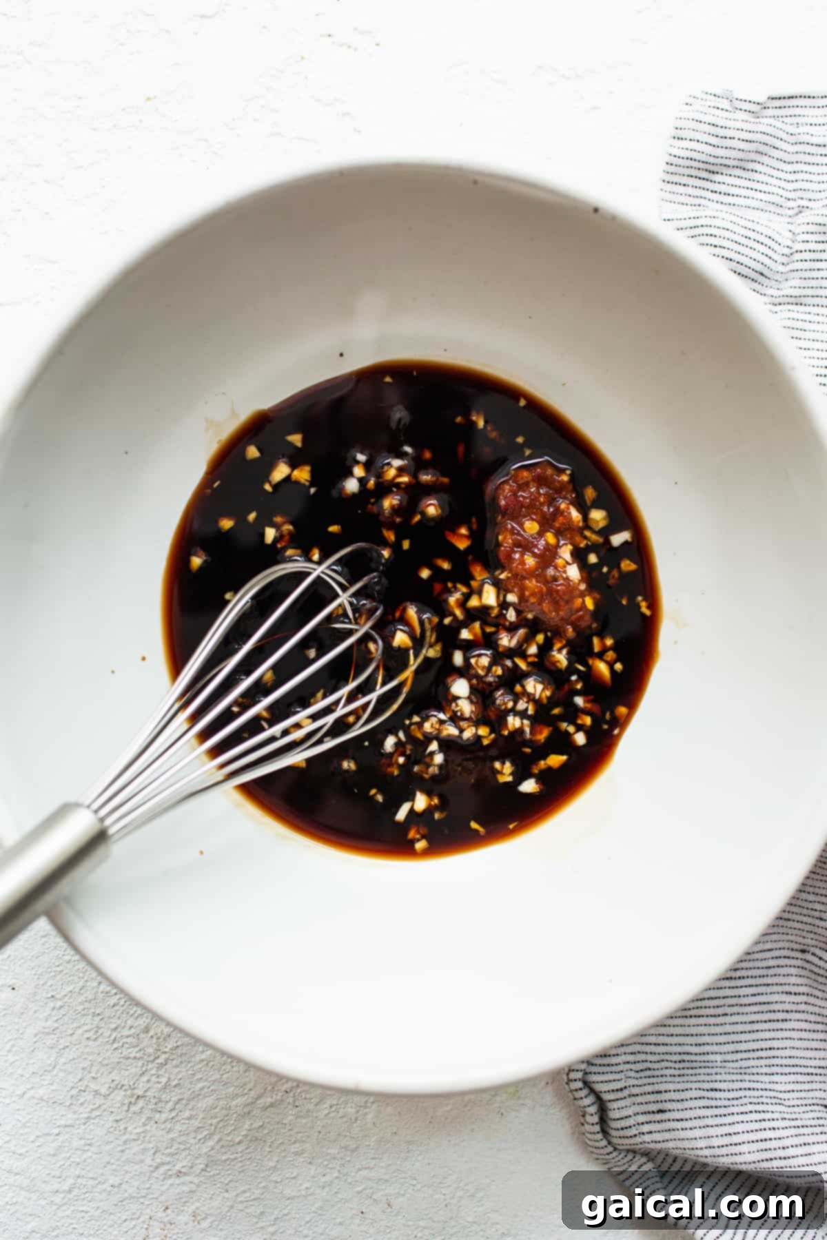 A small white bowl containing a rich, dark stir-fry sauce, garnished with finely chopped green onions.