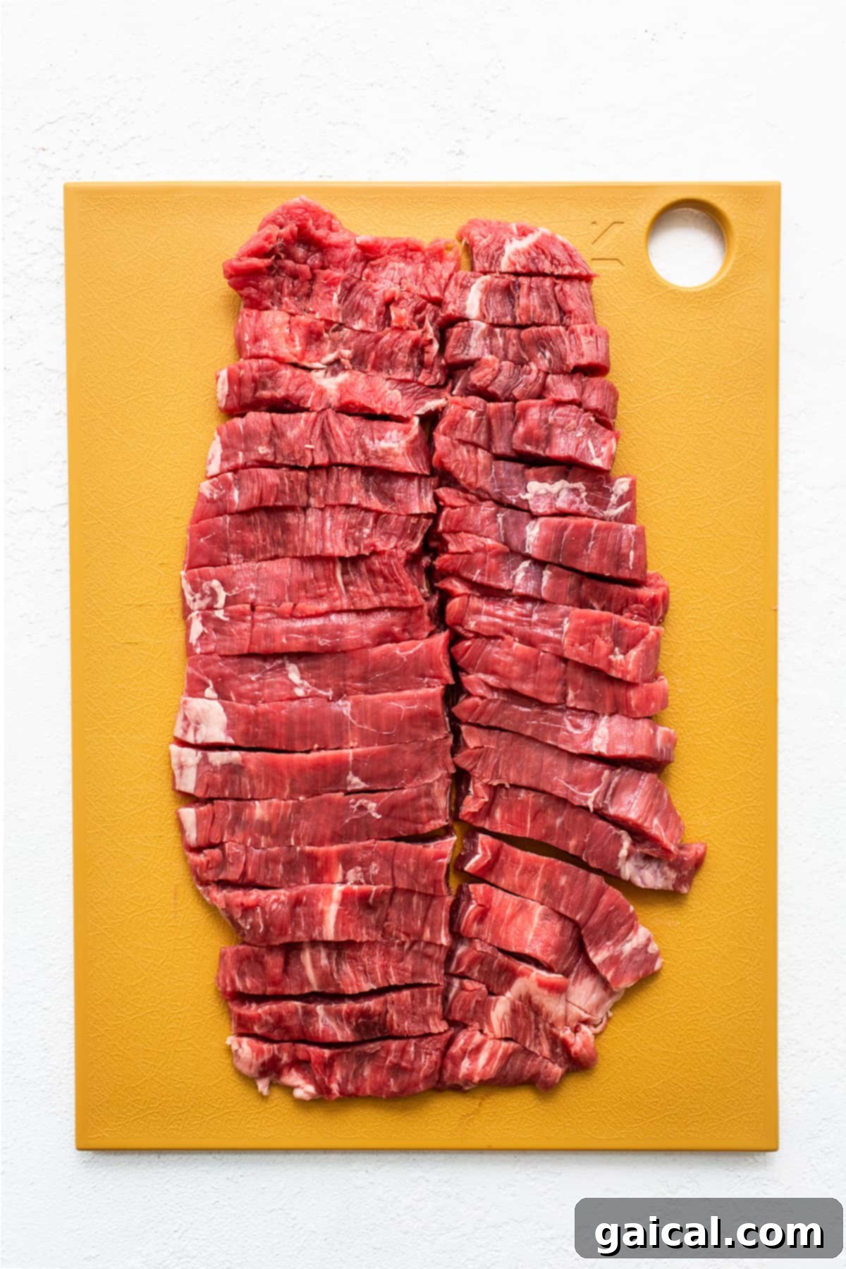 Thinly sliced flank steak strips laid out on a cutting board, ready for cooking.