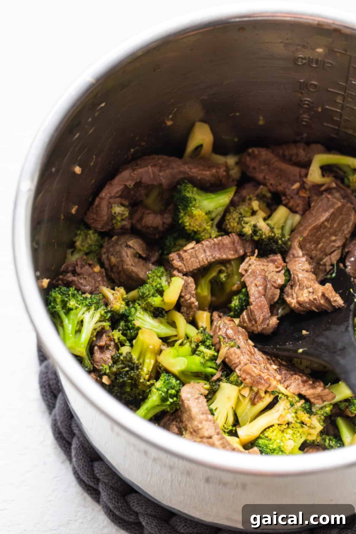 Cooked beef and bright green broccoli florets nestled in a rich sauce inside the Instant Pot.
