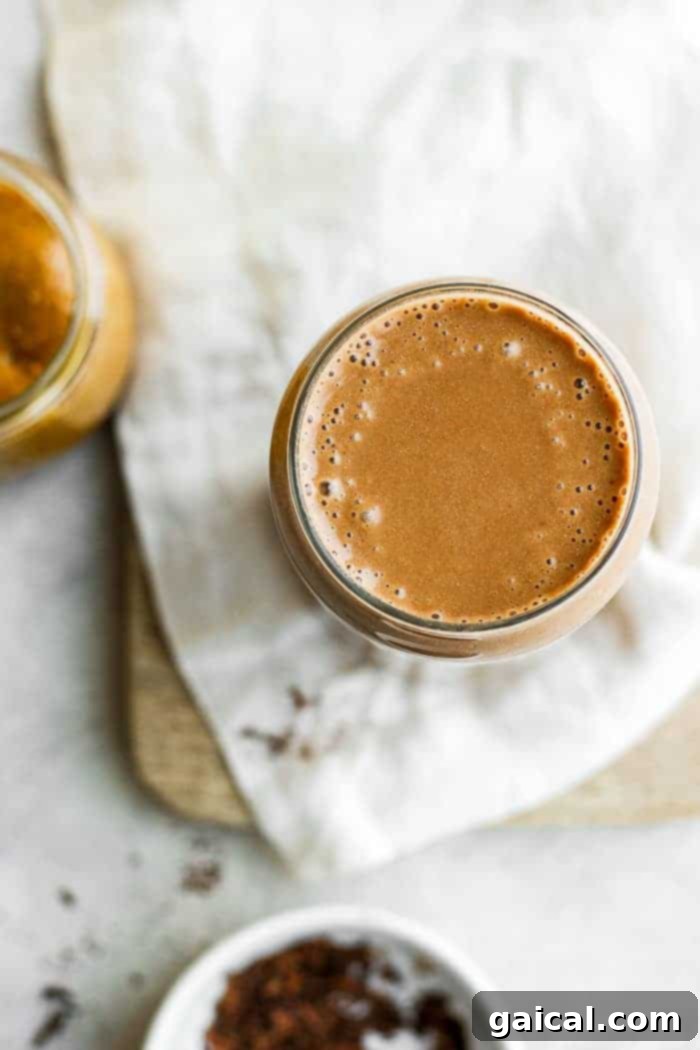 A glass of coffee protein smoothie on a marble counter next to coffee beans