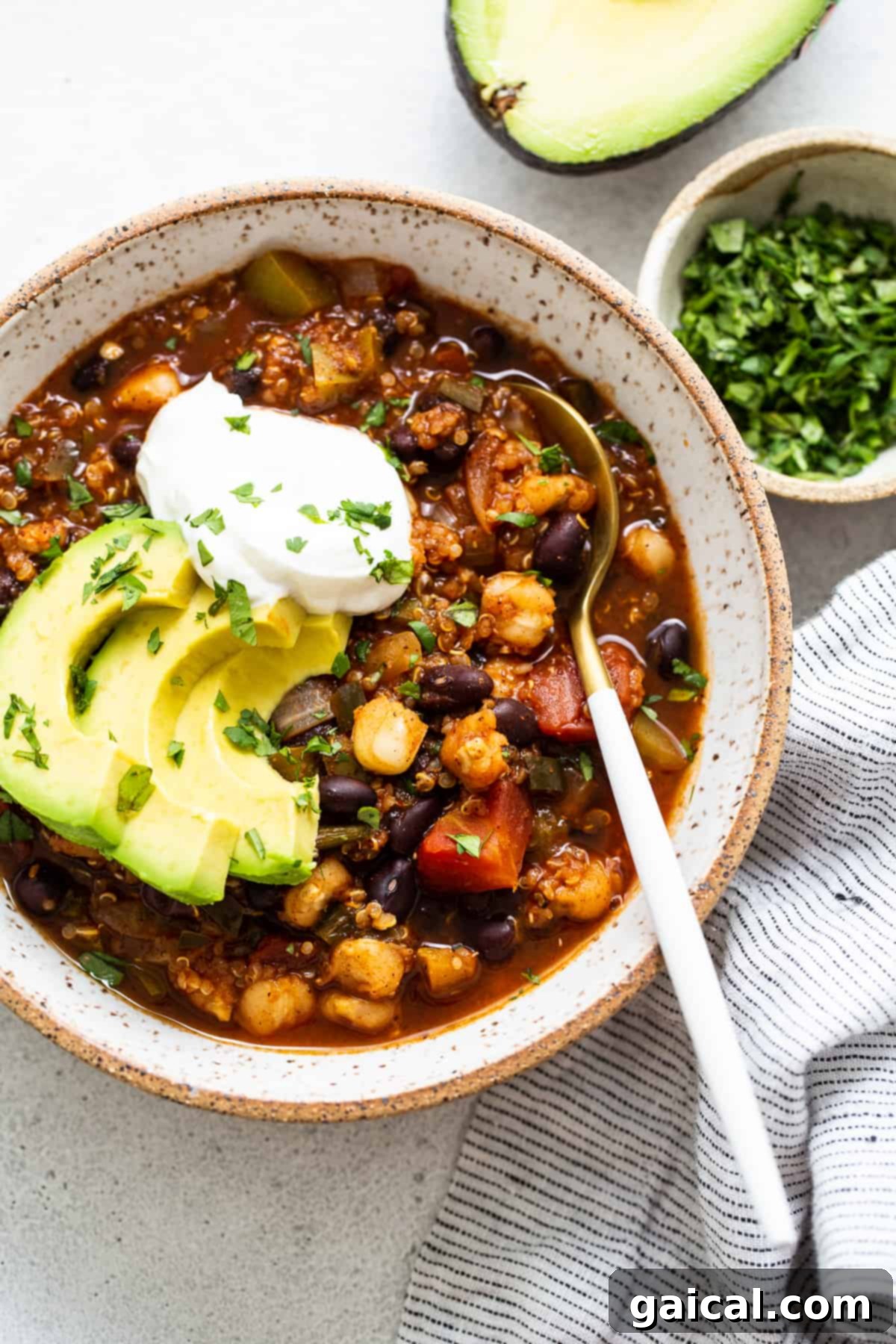 Hearty One-Pot Black Bean Quinoa Chili topped with creamy avocado and cool sour cream. A bowl of vibrant black bean quinoa chili, generously topped with creamy avocado slices and a dollop of sour cream or Greek yogurt, highlighting its rich texture and colorful garnishes.