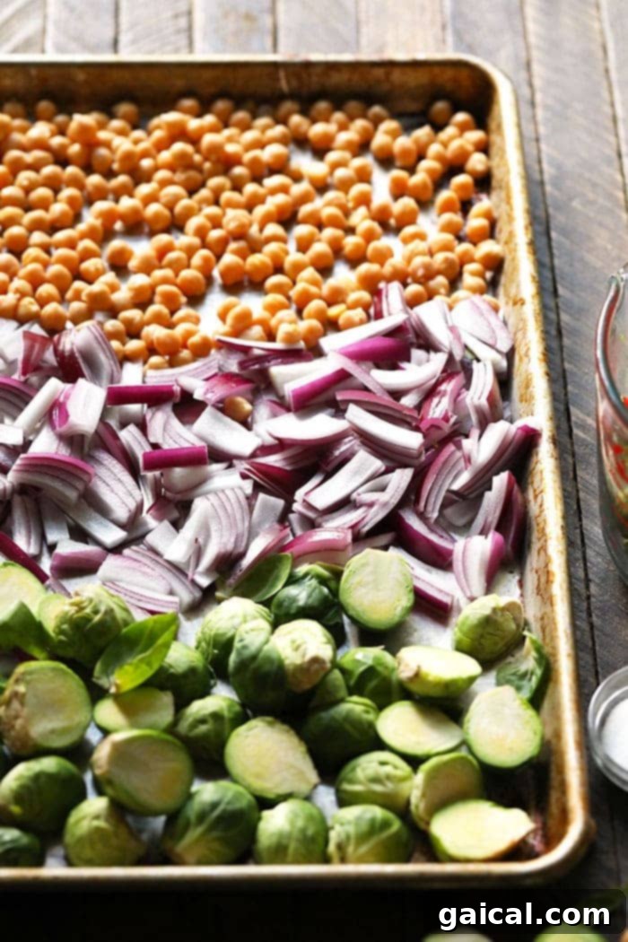 Brussels sprouts, chickpeas, and red onion roasting on a baking sheet
