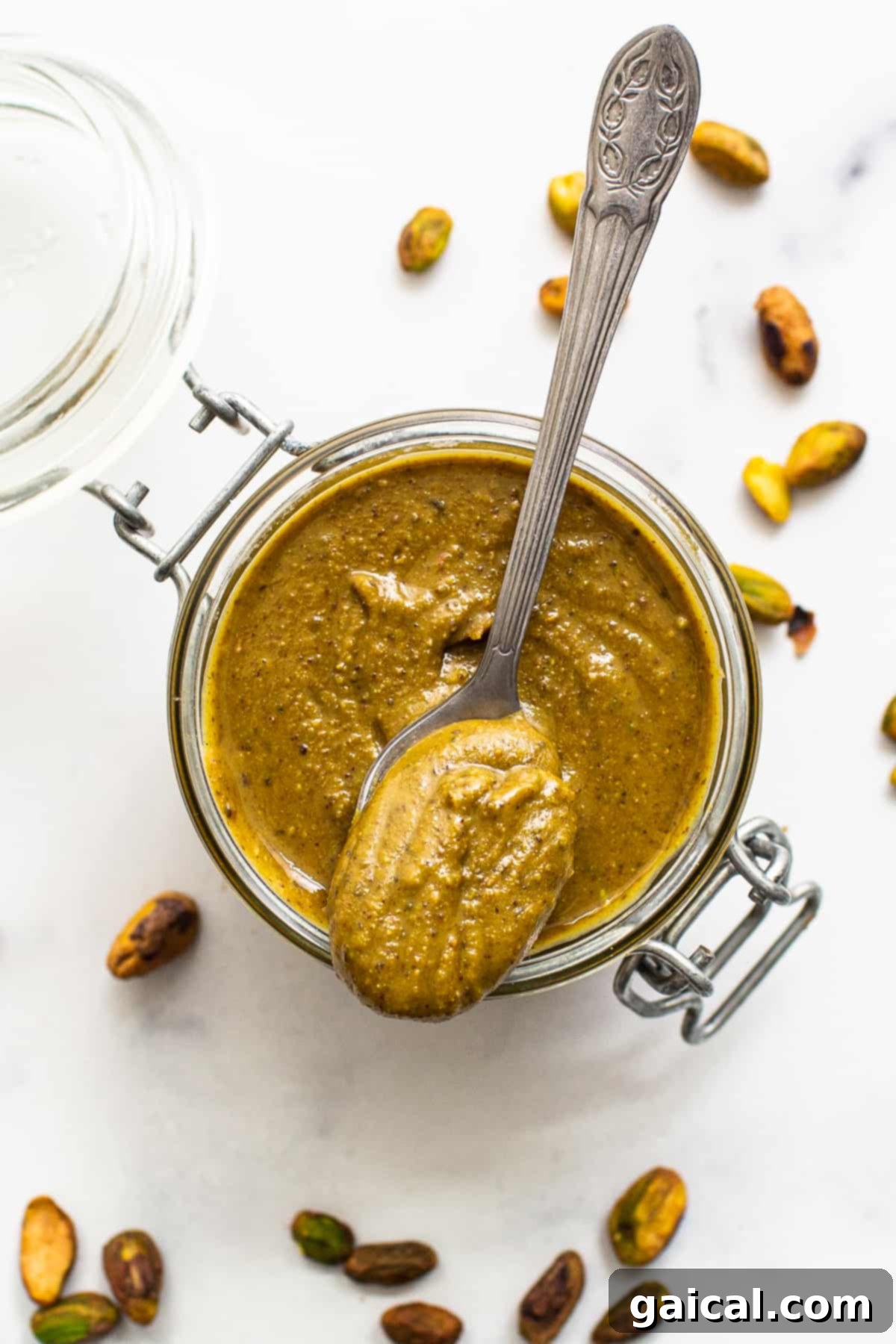 A glass container filled with creamy pistachio butter, garnished with a few whole pistachios.